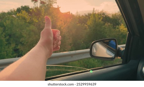 Happy female driver showing like with hand from car window, traveling, playing with sunlight. Car ride on way to vacation. Young female driver playing, catching fresh wind with hand from car window - Powered by Shutterstock