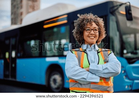 Happy female driver standing with arms crossed at the station and looking away. Copy space.