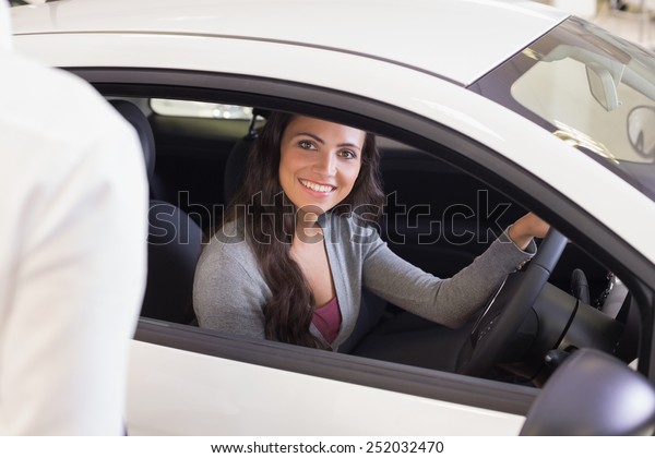 Happy female driver at the wheel sitting in her\
car at new car showroom
