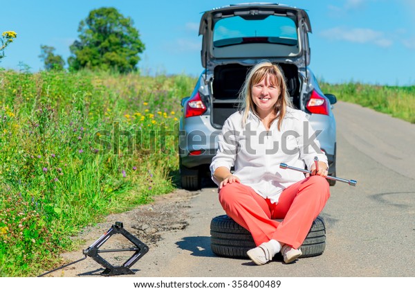 Happy female driver at the wheel sitting near a\
broken car