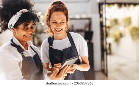 Happy female employees using a mobile app on a tablet to manage the daily operations of their restaurant. Women working together to ensure that customers receive the best hospitality service.