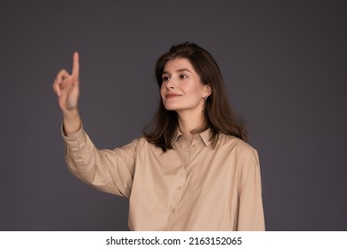 Happy female entrepreneur pushing button on virtual screen over light grey studio background, mockup for design. - Powered by Shutterstock