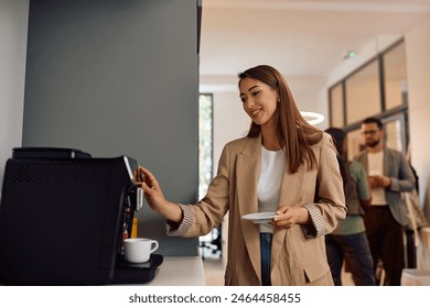 Happy female entrepreneur using coffee maker machine while working in modern office. Copy space.  - Powered by Shutterstock