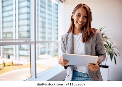 Happy female entrepreneur using touchpad while working in the office and looking at camera. Copy space.