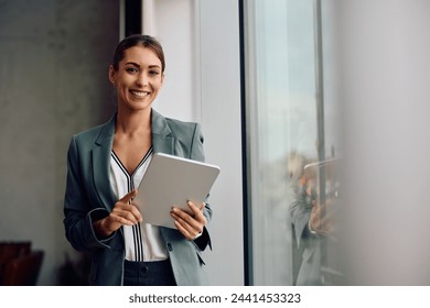Happy female entrepreneur using touchpad while working in the office and looking at camera. Copy space.