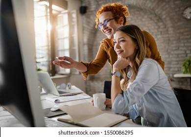 Happy female entrepreneurs reading an e-mail on computer while working together in the office. Focus is on redhead woman. 
