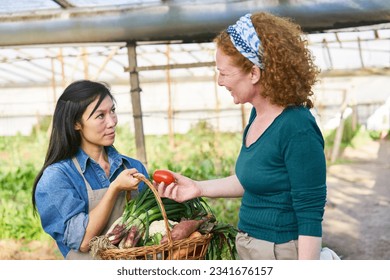 Happy female farmer discussing with mature colleague holding basket of organic vegetables at farm - Powered by Shutterstock