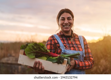 Happy female farmer holding a wood box containing fresh vegetables - Powered by Shutterstock