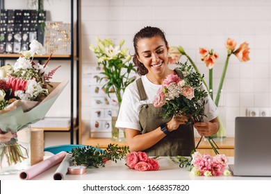 Happy female florist preparing a bouquet in her shop. Smiling woman holding flowers at counter. - Powered by Shutterstock