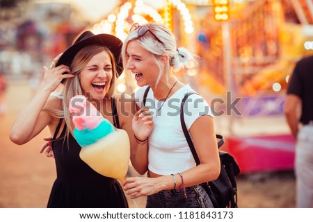 Happy female friends in amusement park eating cotton candy. Two young women enjoying a day at amusement park.