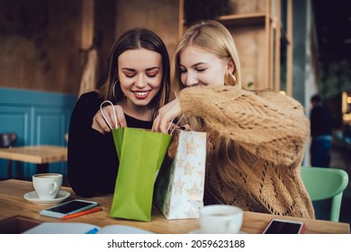 Happy female friends in casual clothes smiling and receiving presents from each other while sitting at wooden table in cozy cafe - Powered by Shutterstock