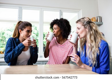 Happy Female Friends Drinking Coffee While Sitting At Table In House