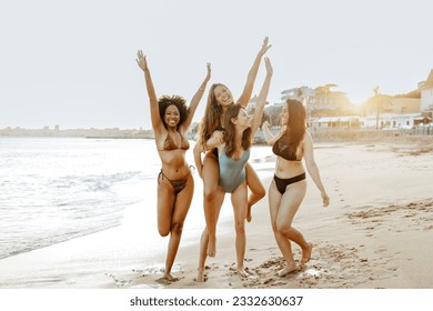 Happy female friends piggybacking each other on the beach, women smiling cheerfully while having fun on coastline. Best friends enjoying their vacation together - Powered by Shutterstock
