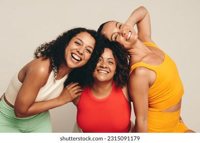 Happy female friends smiling at the camera, celebrating a healthy lifestyle of sport, exercise and fitness. Group of young sportswomen standing together in a studio wearing fitness clothing. Stock fotografie