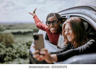 Happy female friends using smartphone to selfies on road trip. Diverse friends traveling and taking selfies by smartphone. Happy women road trip together. Traveling and taking selfies by smartphone. - Powered by Shutterstock