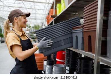 Happy Female Garden Center Worker In Uniform Taking Flower Pots From Shelf