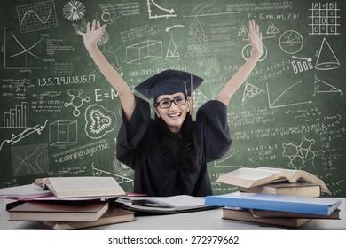 Happy Female Grad Raised Her Arms In Classroom With Books And Laptop