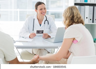 Happy female gynaecologist talking to expectant couple in clinic