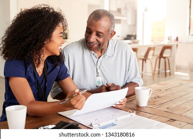 Happy Female Healthcare Worker Sitting At Table Smiling With A Senior Man During A Home Health Visit