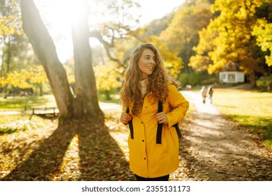 Happy female hiker in yellow coat walking in golden autumn forest. Beautiful woman has fun in autumn in the park. Trips. Active lifestyle. - Powered by Shutterstock