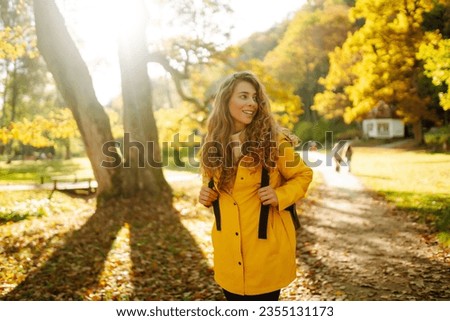 Happy female hiker in yellow coat walking in golden autumn forest. Beautiful woman has fun in autumn in the park. Trips. Active lifestyle.