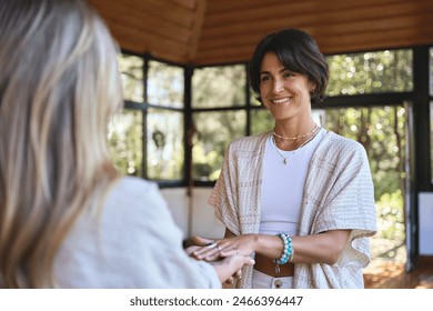 Happy female holistic teacher holding hands of woman during spiritual practice meditation experience feeling energy, peace and love, giving support during body health retreat healing training session. - Powered by Shutterstock