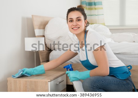 Happy Female Housekeeper Cleaning Nightstand In Room