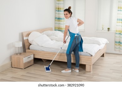 Happy Female Housekeeper Mopping Hardwood Floor In Room