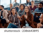 Happy female manager asking a question from the audience while participating in business seminar at convention center.