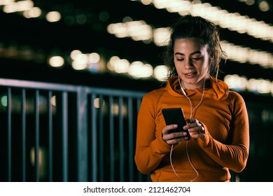 A happy female night runner is using the phone for music on a city street. - Powered by Shutterstock