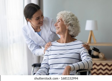 Happy female nurse or caregiver talk support positive handicapped old lady patient sitting in wheelchair in hospital, young woman doctor give help take care of mature handicapped grandmother