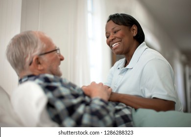 Happy Female Nurse Comforting An Elderly Patient At His Bedside.