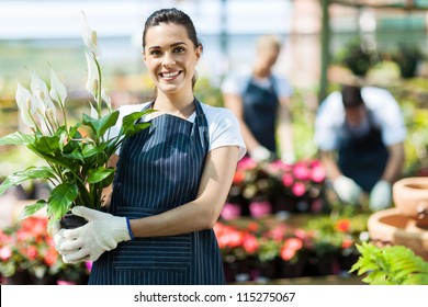 happy female nursery owner with pot of flowers inside greenhouse