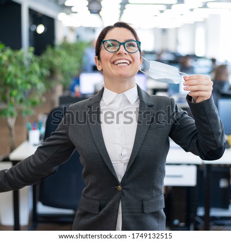 A happy female office worker in a suit takes off her medical mask and breathes freely with full breasts. A smiling woman takes off virus protection. End of quarantine. Victory over the coronavirus.