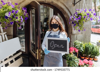 Happy female owner holding open sign while wearing protective face mask and gloves at floral shop's doorway. - Powered by Shutterstock