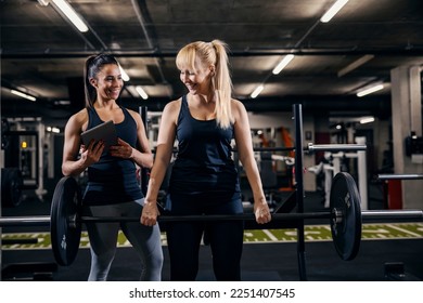 A happy female personal trainer with tablet is training sportswoman who is doing strength exercises in a gym. - Powered by Shutterstock