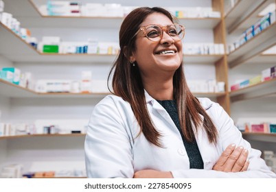 Happy female pharmacist standing in a drug store with crossed arms. Mature woman working in a pharmacy. Female healthcare worker in a chemist. - Powered by Shutterstock
