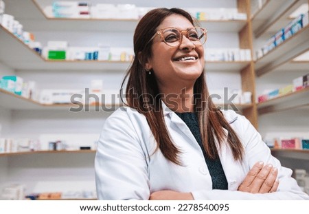 Happy female pharmacist standing in a drug store with crossed arms. Mature woman working in a pharmacy. Female healthcare worker in a chemist.