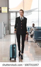 happy female pilot with suitcase walking by airport lobby