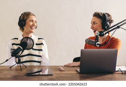 Happy female podcasters having a great conversation on an audio broadcast in a home studio. Two cheerful women recording an internet podcast for their social media channel. - Powered by Shutterstock