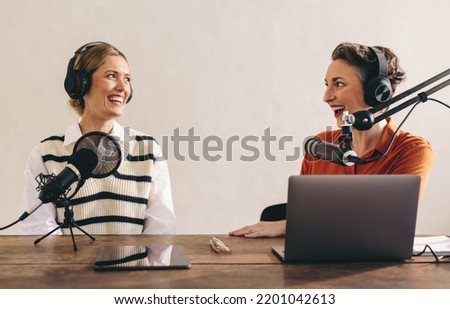 Happy female podcasters having a great conversation on an audio broadcast in a home studio. Two cheerful women recording an internet podcast for their social media channel.