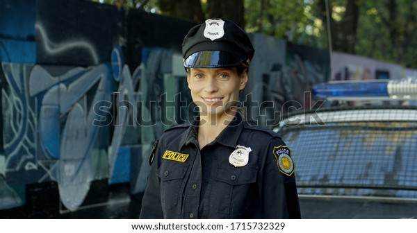 Happy female police officer with his patrol\
car in the background.