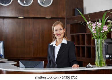 Happy Female Receptionist Standing At Hotel Counter