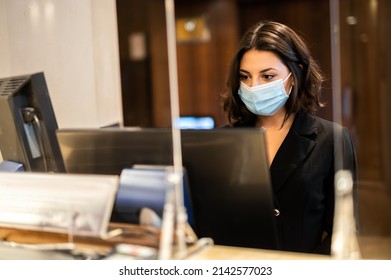 Happy female receptionist standing at hotel counter wearing masks to protect from covid 19 coronavirus pandemic