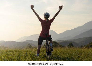 Happy Female Road Cyclist In Joy, With Arms Raised Above Her Head Looking At Sunset