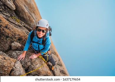Happy female rock climber looking at the camera from a rock face wall above the clouds