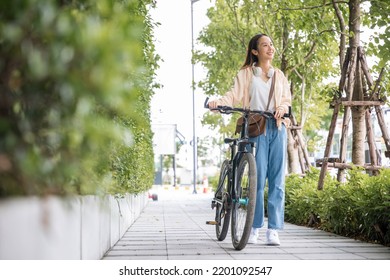 Happy female smiling walk down the street with her bike on city road, ECO environment, healthy holiday travel, Asian young woman walking alongside with bicycle on summer in park countryside outdoor - Powered by Shutterstock