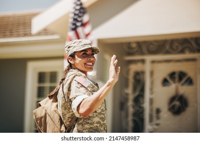 Happy female soldier smiling and waving her hand proudly while standing outside her home. Patriotic American servicewoman coming back home after serving her country in the military.