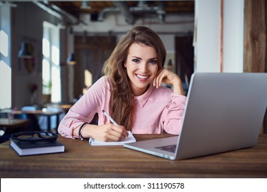 Happy Female Student At Cafe With Laptop And Notepad Doing Some Homework