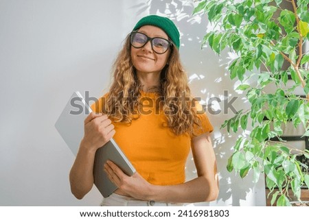 Happy female student with laptop. Young girl near green flower on white background smiling looking at camera and holding portable computer in hands. Geek, nerd, studious woman. Online college concept